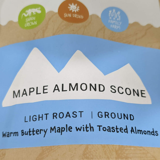 Velasquez Family Coffee Maple Almond Scone flavored coffee. Image of coffee bag label for Maple Almond Scone coffee, light roast, ground, Warm Buttery Maple with Toasted Almonds description.