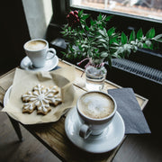 Sugared Snowflake flavored coffee sweet, warm buttery sugar cookie fresh from the oven. Image of frosted snowflake cookie with two cups of coffee and holiday greens.