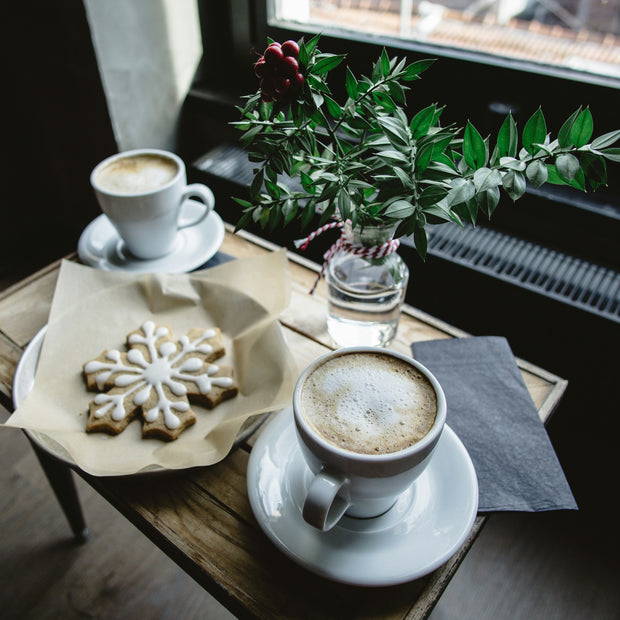 Sugared Snowflake flavored coffee sweet, warm buttery sugar cookie fresh from the oven. Image of frosted snowflake cookie with two cups of coffee and holiday greens.