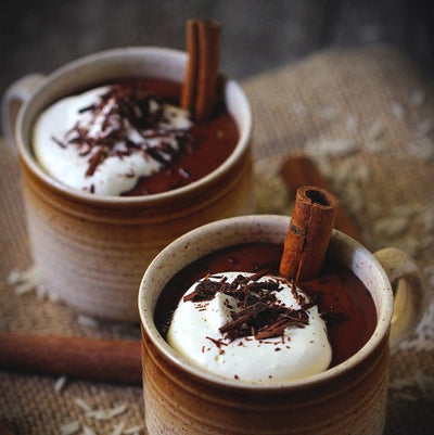 Mugs of hot cocoa topped with whipped cream, chocolate sprinkles with a cinnamon stick